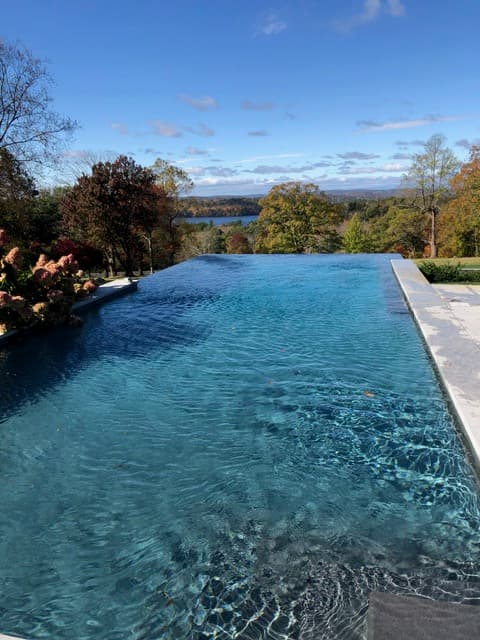 An infinity-edge pool overlooking a lake in fall foliage, serviced by River Valley Pools